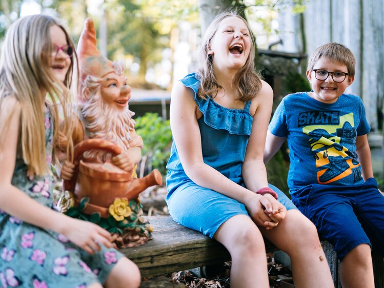 Kinder lachen auf einer Bank neben einem Gartenzwerg | © Urlaub am Bauernhof Oberösterreich / Daniel Gollner