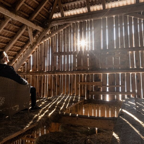 Der Dachboden im Ferienhaus mit Holzbalken, natürlichem Lichteinfall und einem Sitzbereich auf Stroh.