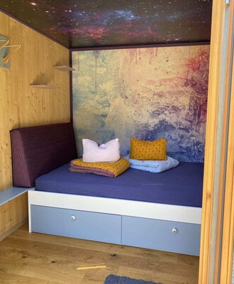 Schlafbox mit einem Bett mit integrierten Schubladen, Holzwänden und einer Decke mit Sternenmuster.