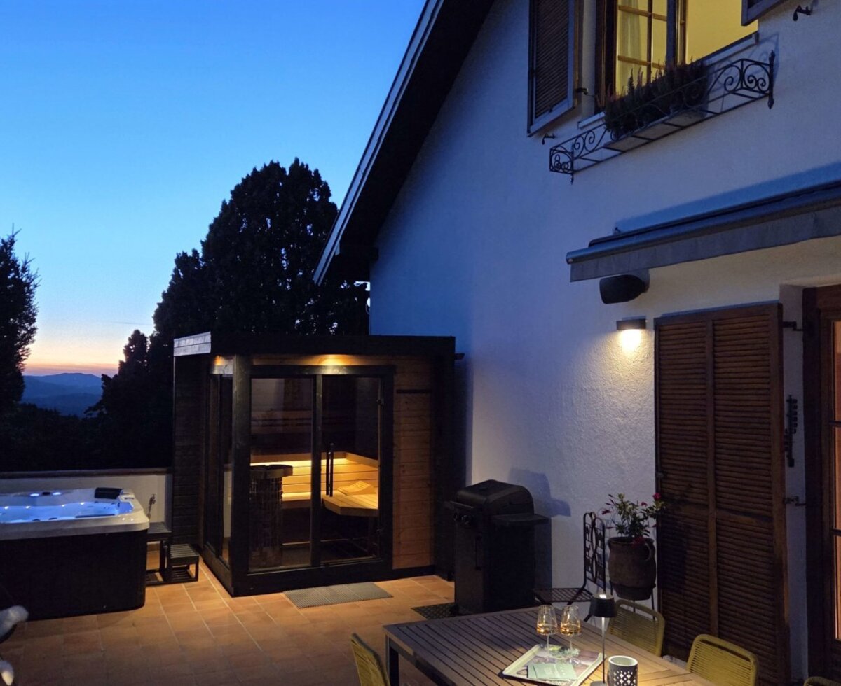 Die Terrasse in Abendstimmung ausgestattet mit einem Whirlpool, einer Sauna und einem Essbereich im Freien.