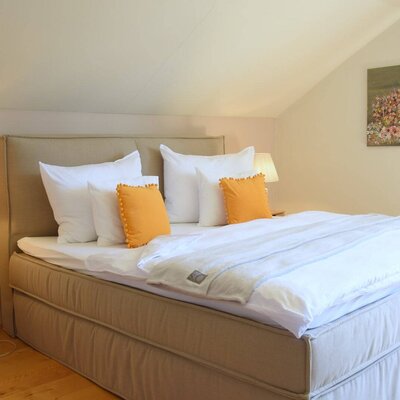 Doppelzimmer im Bauernhof mit Boxspringbett, Nachttischen, Leselampen und einer Dachschräge.
