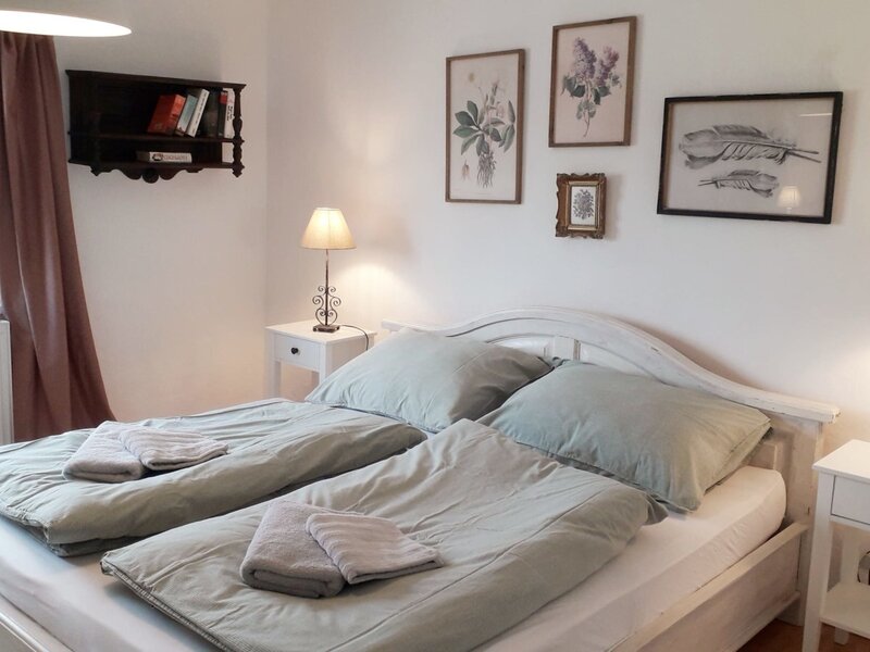 Schlafzimmer der Unterkunft mit Doppelbett, zwei Nachttischen, Leselampen, frischen Handtüchern und Fenster.