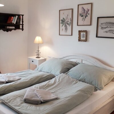 Schlafzimmer der Unterkunft mit Doppelbett, zwei Nachttischen, Leselampen, frischen Handtüchern und Fenster.