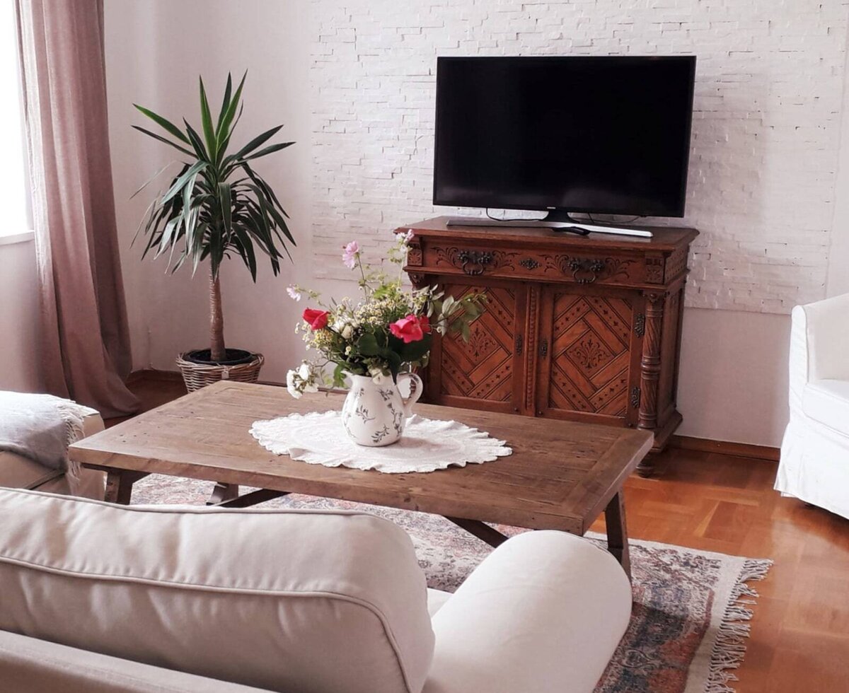 Wohnbereich in der Unterkunft mit Fernseher, Holztisch, Sofa und einer Pflanze.