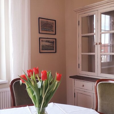 Essbereich in der Unterkunft mit Fenster, Tisch mit frischen Blumen und einem Vitrinenschrank.