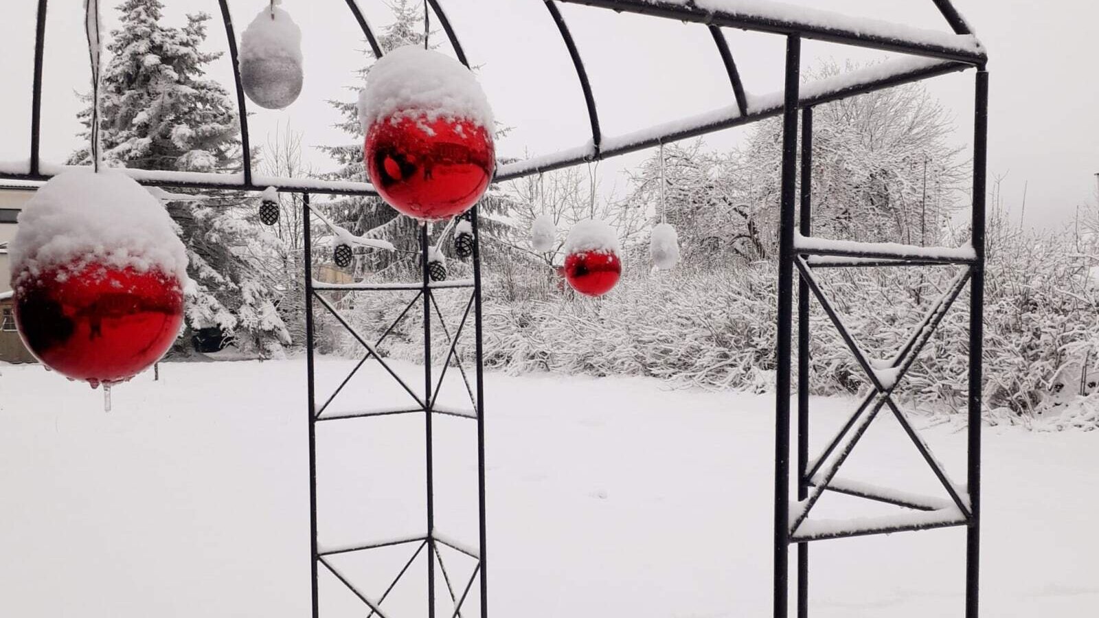 Der verschneite Außenbereich der Unterkunft mit einem Metallbogen, der mit roten und weißen Kugeln dekoriert ist.