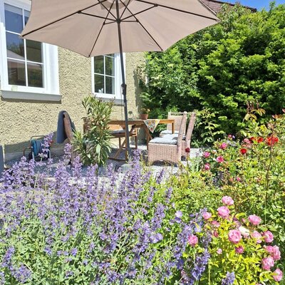 Außenterrasse des Ferienhauses mit Tisch, Stühlen, Sonnenschirm und blühendem Garten.