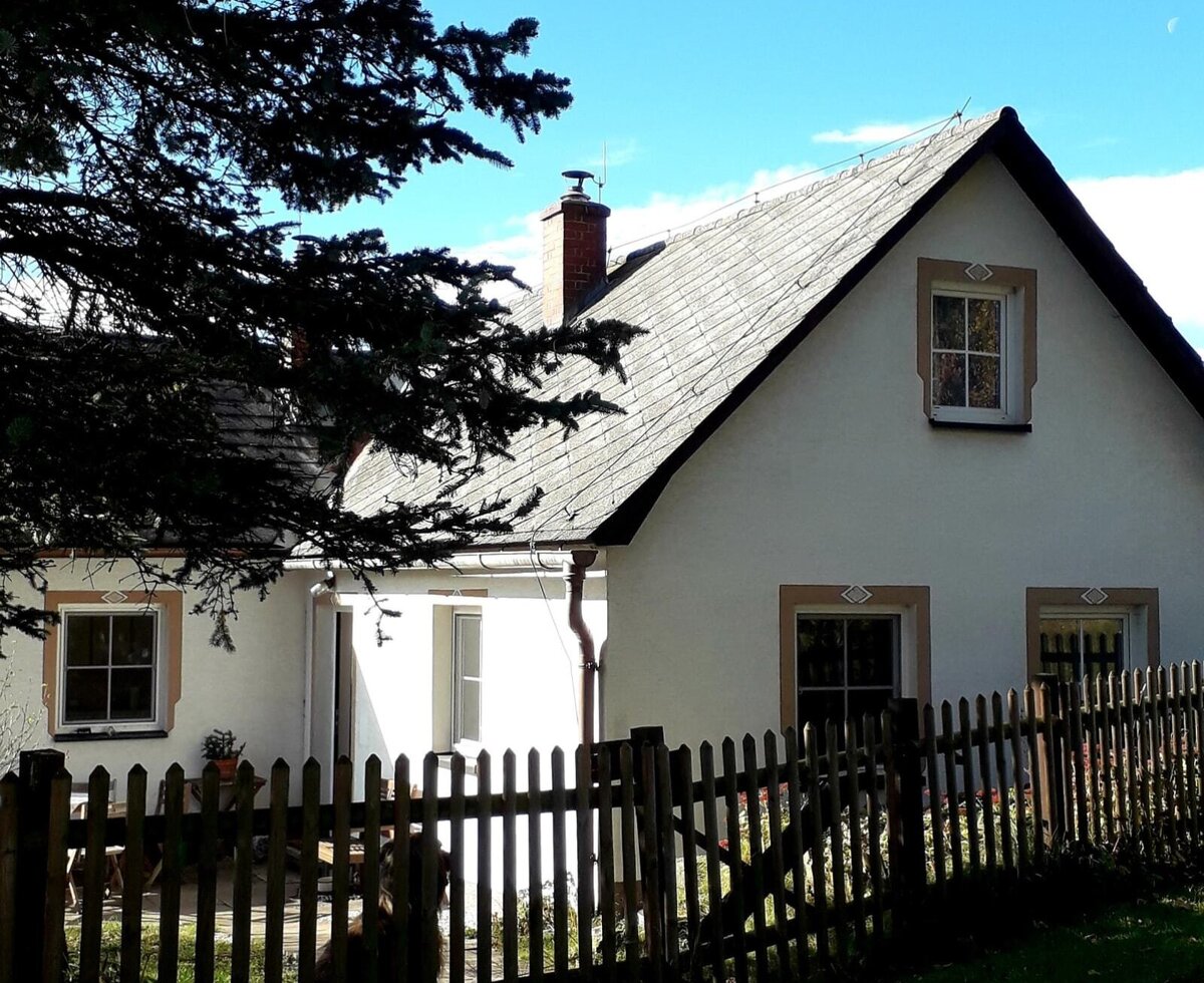 Außenansicht des Ferienhauses mit weißer Fassade, dunklem Dach und Holzzaun.