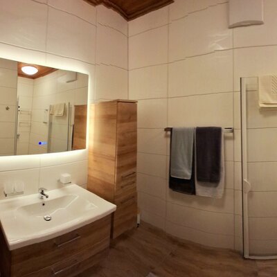 Das Badezimmer im Bauernhof verfügt über einen Waschtisch mit beleuchtetem Spiegel, Holzschränke und eine begehbare Dusche.