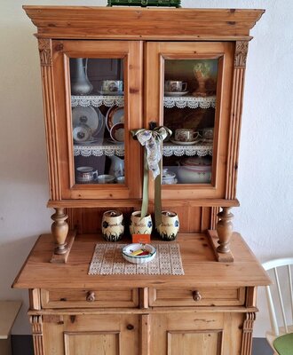 Traditioneller Holzschrank im Bauernhof, bestückt mit Geschirr und einer dekorativen Waage.