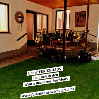 Die beleuchtete Terrasse des Ferienhauses am Abend mit Rasenfläche im Vordergrund.