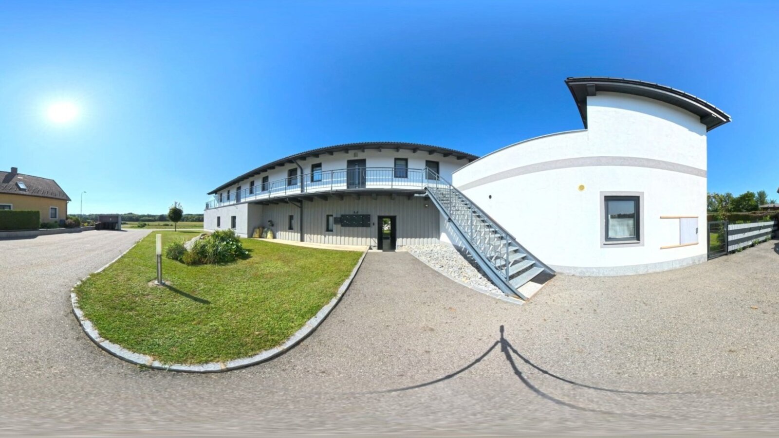 Der einladende Außenbereich des Hauses mit einem gepflegten Rasen und modernen Gebäuden unter strahlend blauem Himmel.