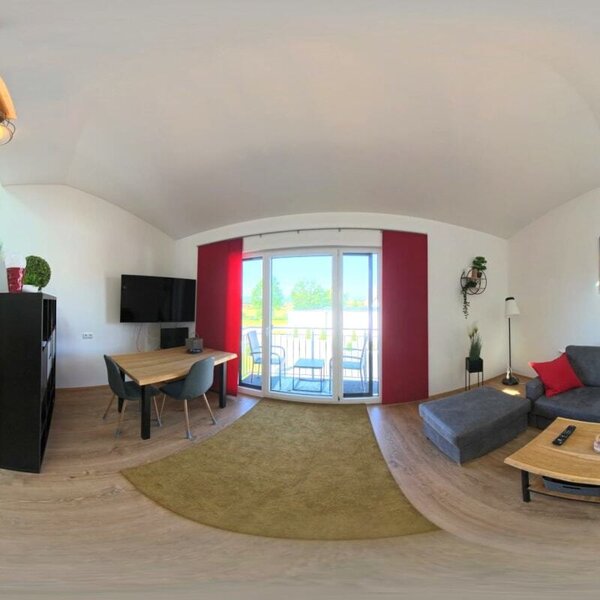 Der lichtdurchflutete Wohnbereich des Hauses bietet eine moderne Küchenzeile, eine gemütliche Sofaecke und Zugang zum Balkon.