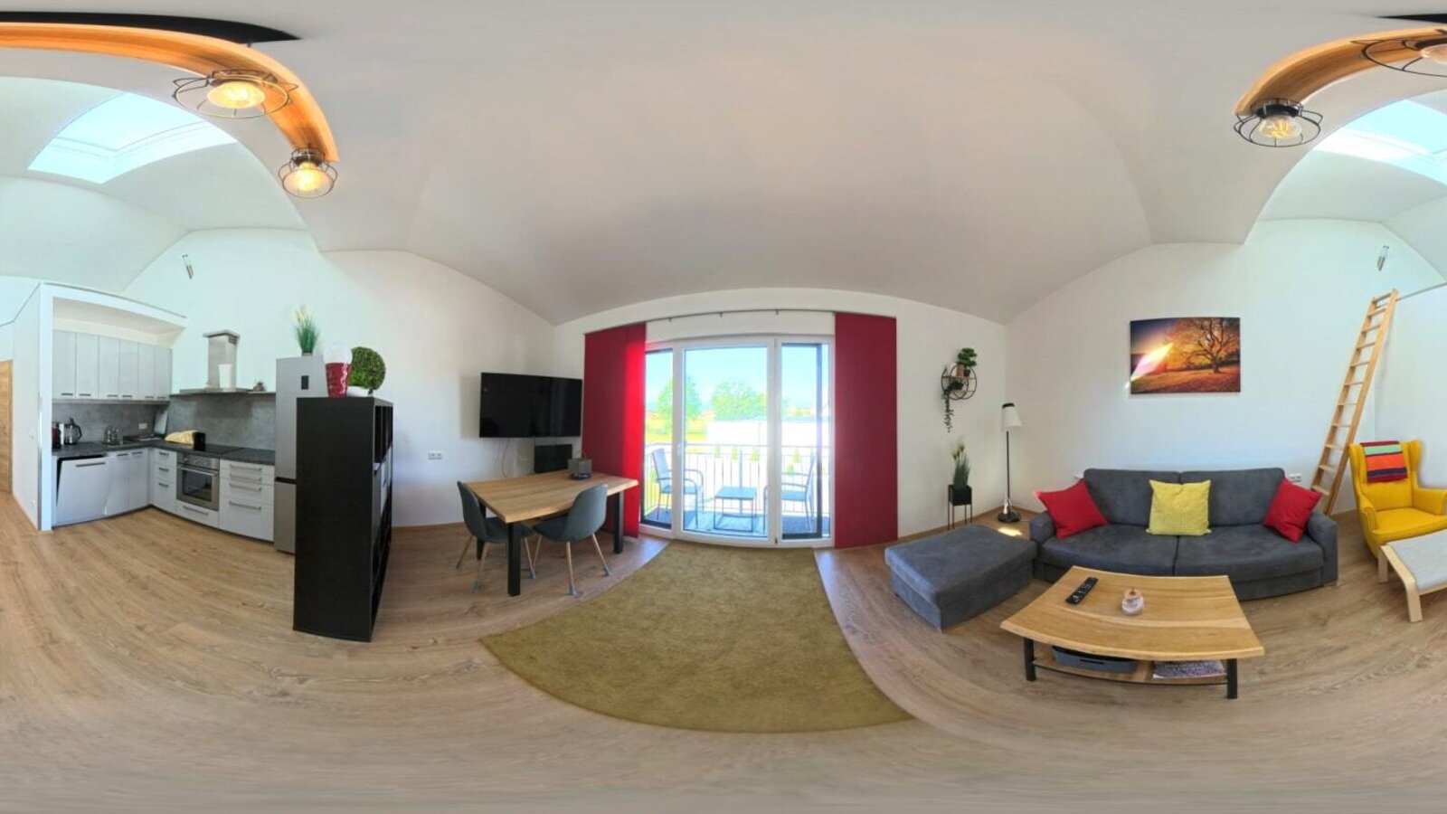 Der lichtdurchflutete Wohnbereich des Hauses bietet eine moderne Küchenzeile, eine gemütliche Sofaecke und Zugang zum Balkon.