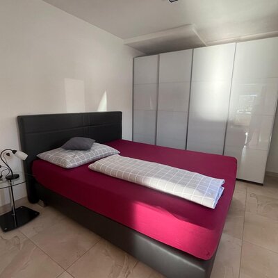 Schlafzimmer mit Doppelbett, Nachttisch und weißem Kleiderschrank.