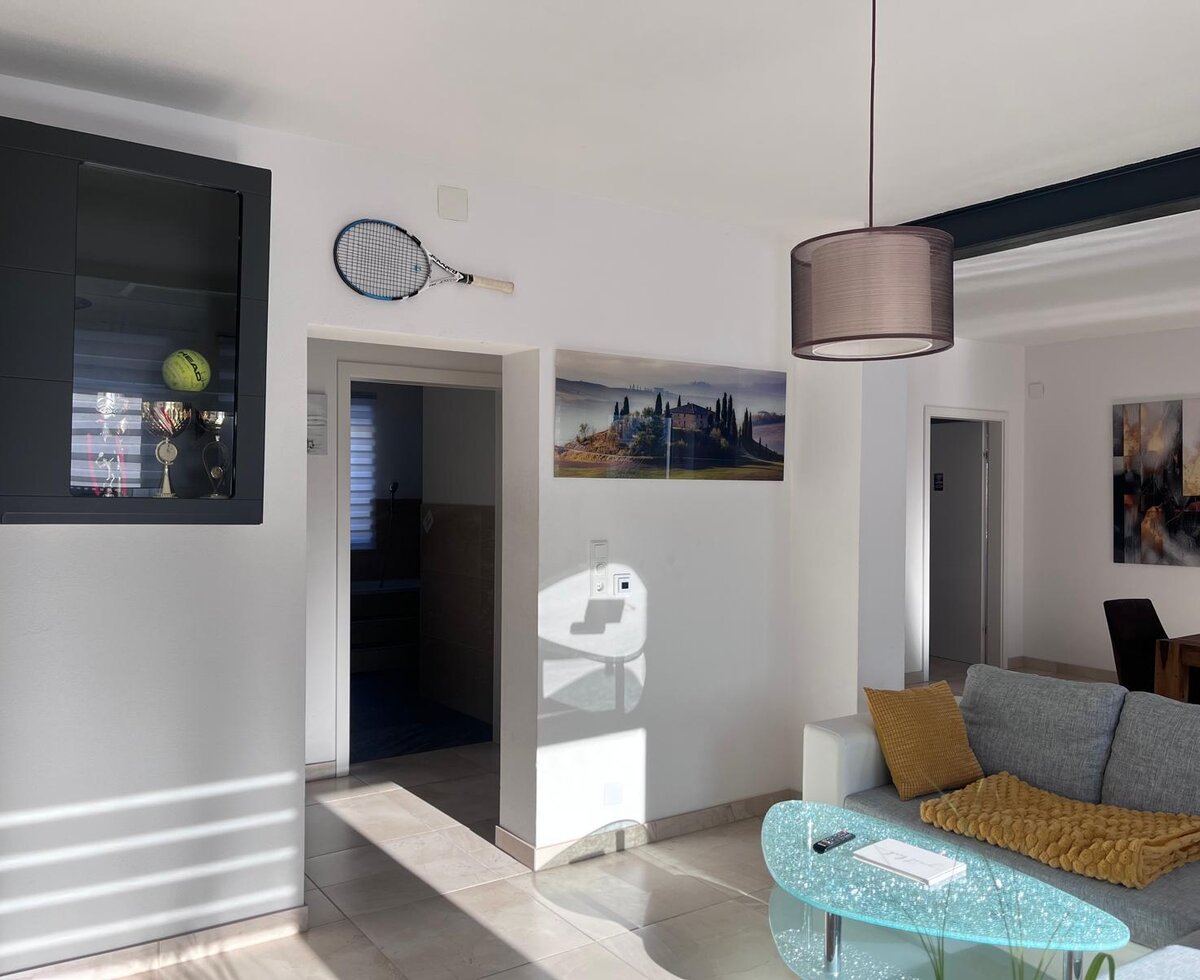 Wohnbereich mit Sofa, Couchtisch und einer Vitrine mit Tennis-Trophäen und einem Schläger.