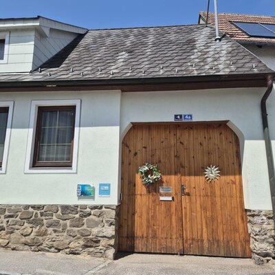 Außenansicht des Bauernhofs mit weißer Fassade, Steinsockel, großen Holztüren und Schindeldach.