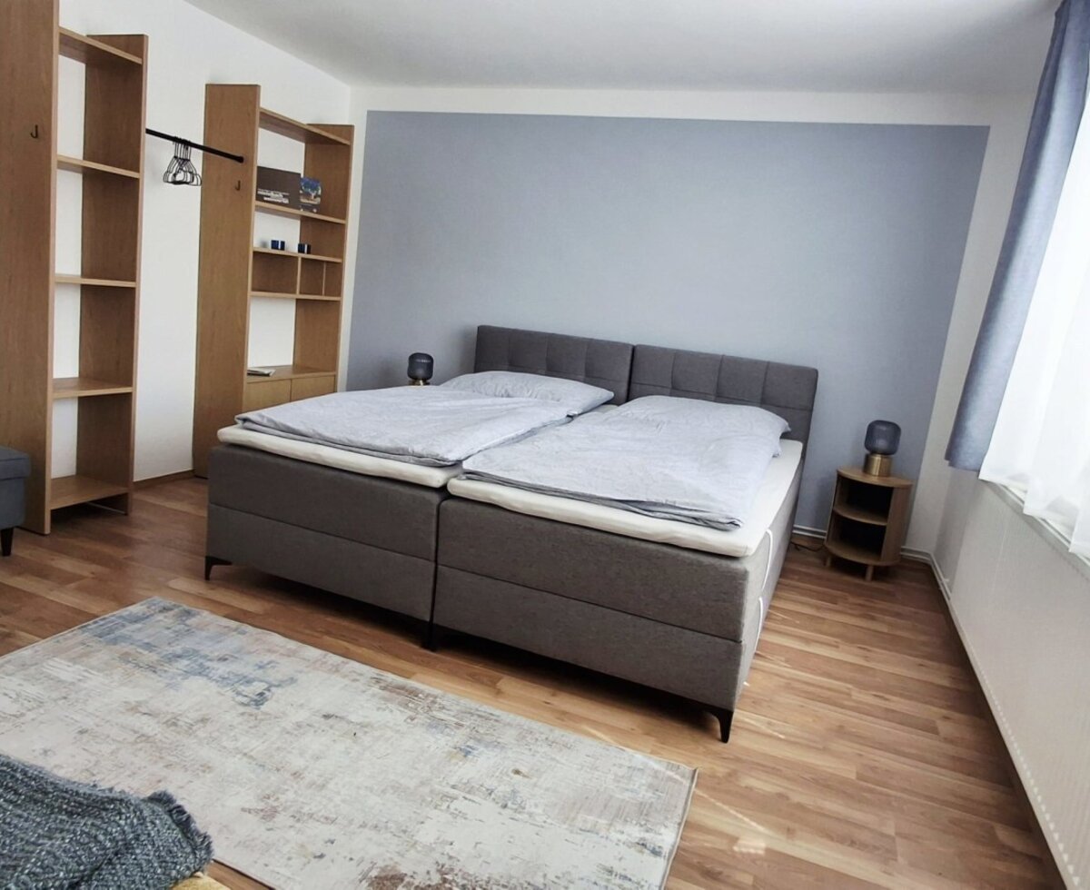 Ein einladendes Schlafzimmer im Haus mit einem komfortablen Doppelbett, stilvollen Holzregalen und wohnlichen Holzböden.