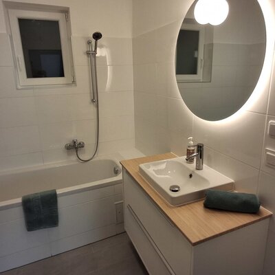 Ein modernes Badezimmer im Haus mit einer einladenden Badewanne, einem stilvollen Waschtisch und einem warm hinterleuchteten, runden Spiegel.