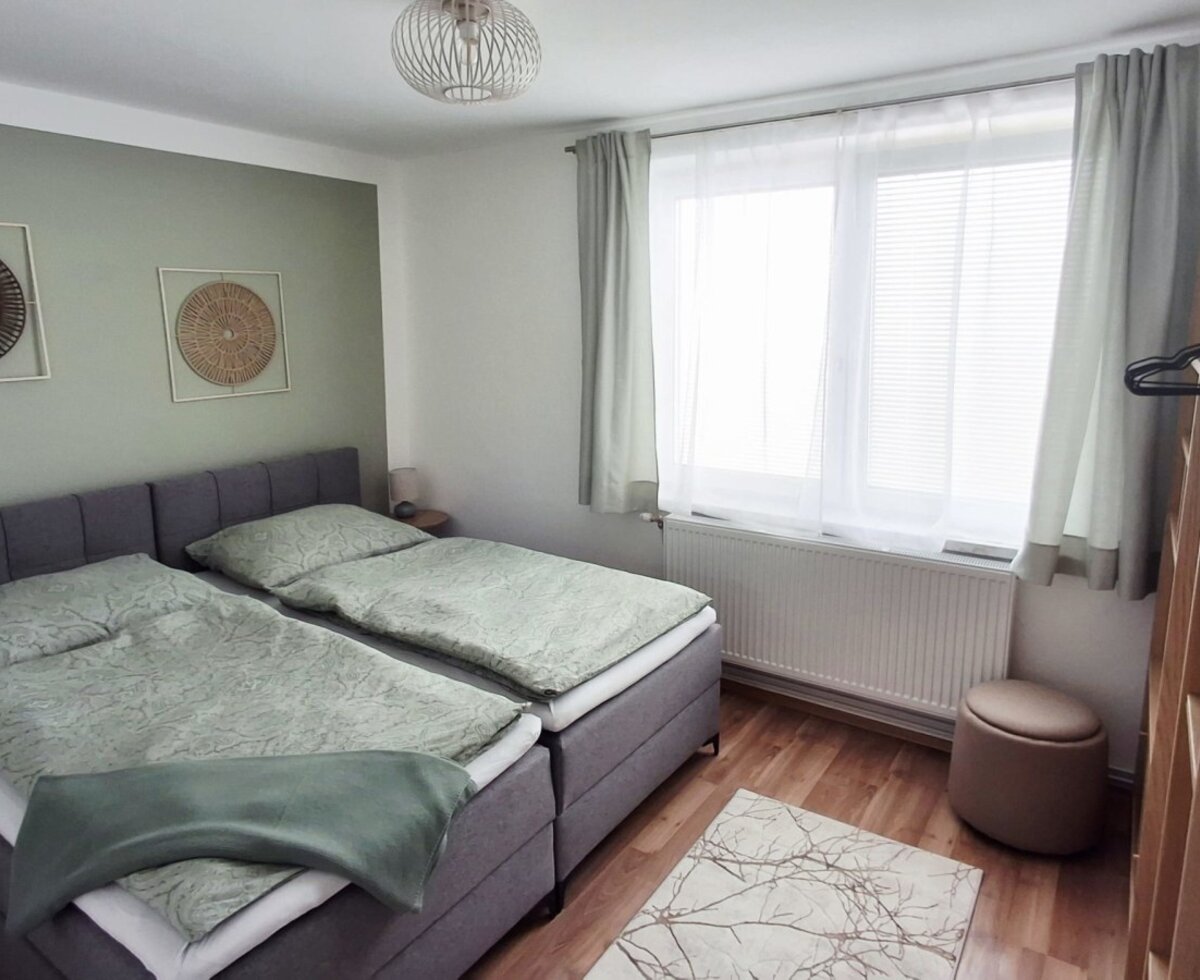 Ein gemütliches Schlafzimmer des Hauses mit bequemen Betten, harmonischen Grüntönen und viel natürlichem Licht durch das große Fenster.