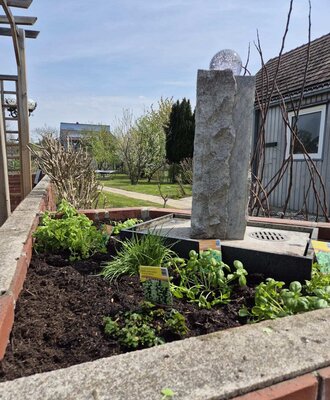 Ein gepflegtes Kräuterbeet des Bauernhofs mit einem dekorativen Steinbrunnen und Blick auf den grünen Garten.