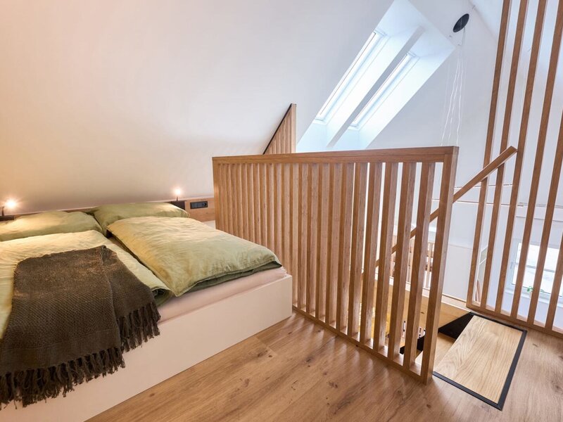 Schlafbereich im Haus mit Doppelbett, zwei Dachfenstern und Holzgeländer auf der oberen Ebene.