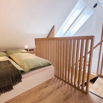 Schlafbereich im Haus mit Doppelbett, zwei Dachfenstern und Holzgeländer auf der oberen Ebene.
