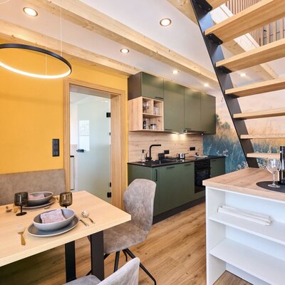 Kombinierter Essbereich und Küche im Haus mit Holzbalken, moderner Treppe und gelber Akzentwand.