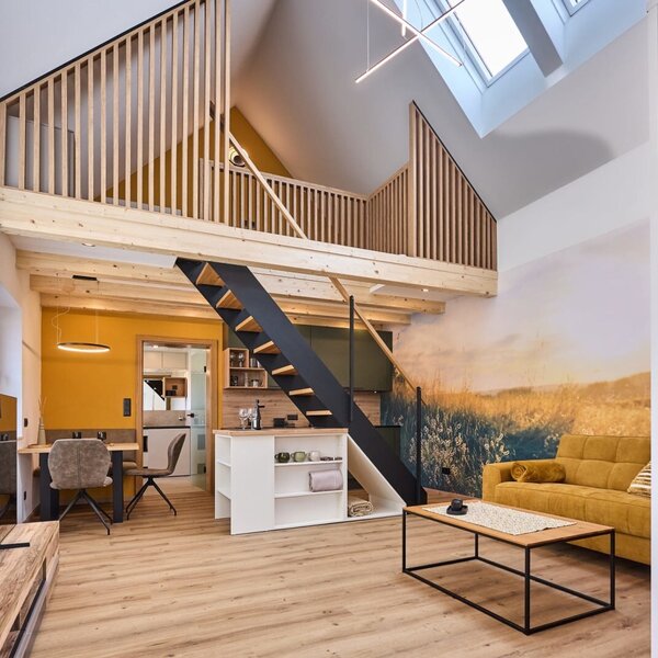 Der offene Wohnbereich im Haus mit einer Galerie, die über eine Treppe erreichbar ist, einem Sofa, Esstisch, einer Küchenzeile und einem Kleiderschrank.