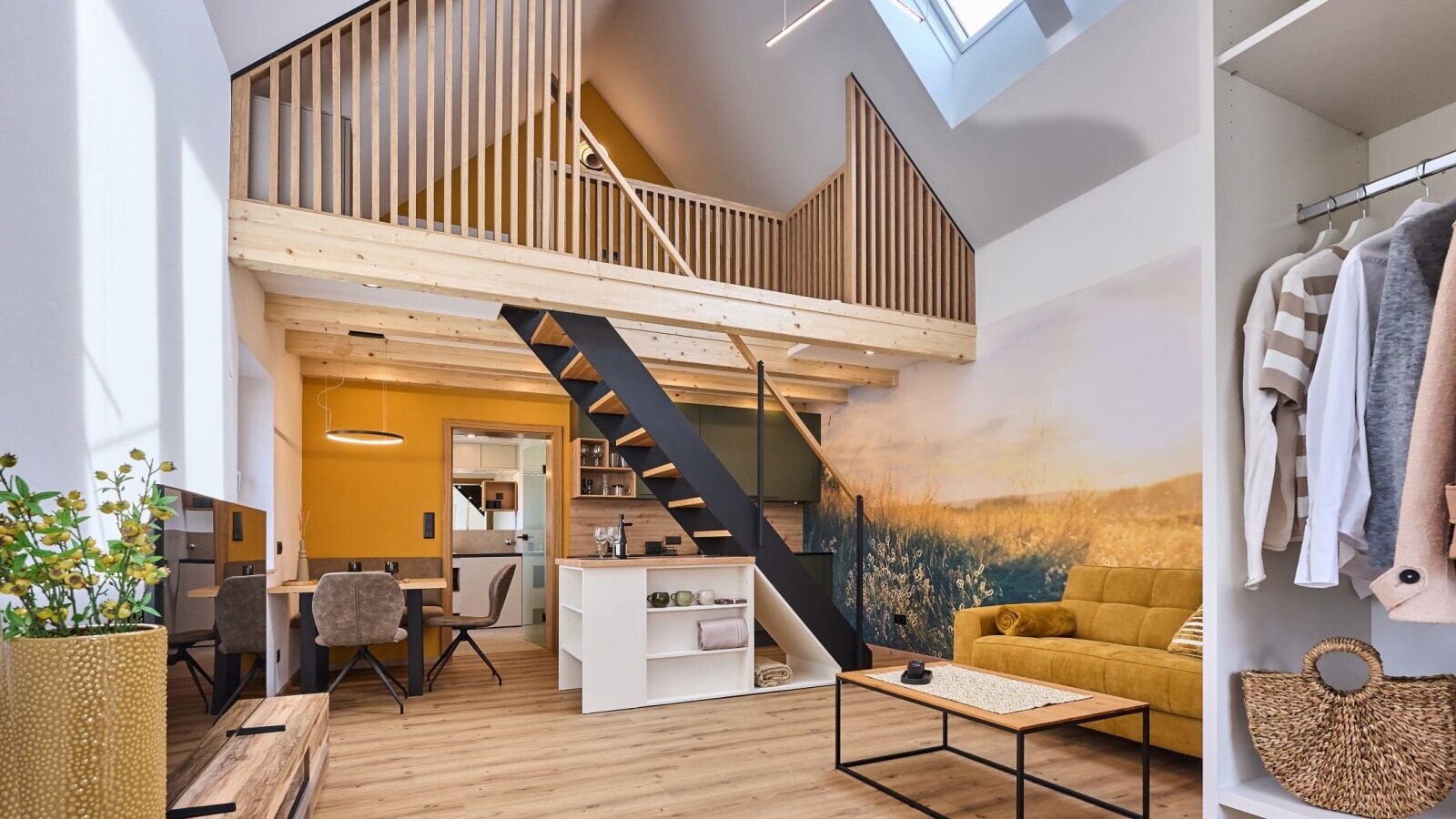 Der offene Wohnbereich im Haus mit einer Galerie, die über eine Treppe erreichbar ist, einem Sofa, Esstisch, einer Küchenzeile und einem Kleiderschrank.