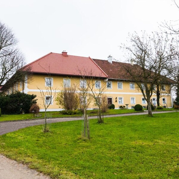 Der Hof Maisserhof, ein Gebäude mit gelber Fassade und roten Dächern, umgeben von einer Grünfläche und Bäumen.